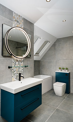 bathroom with wall attached sink and blue drawers square mirror with circular ring light attached, corner bathtub with toilet right next to it