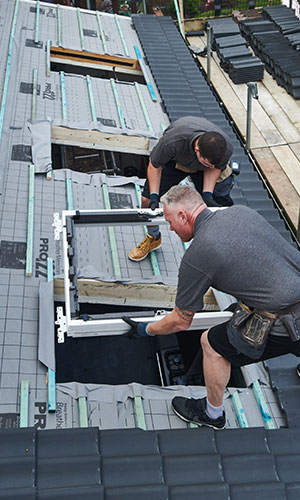 two workers adding rooftop windows to a roof