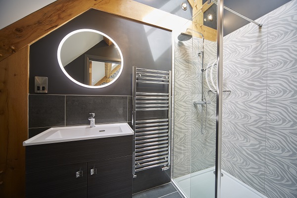 Shower room with wavey grey wall paper modern black walls towel rack sink and cupboard and ring mirror with internal light